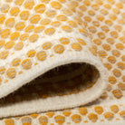 Draped folds of the mustard yellow Theo wool rug highlighting the flexible, soft texture of its geometric pattern