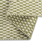 A folded corner of the sage green Theo hand-woven wool rug, showing its dense, chunky wool texture and backing.