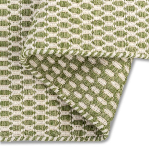 A folded corner of the sage green Theo hand-woven wool rug, showing its dense, chunky wool texture and backing.