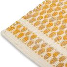 Close-up of the woven edge and border detailing on the mustard yellow and cream Theo hand-woven wool rug.