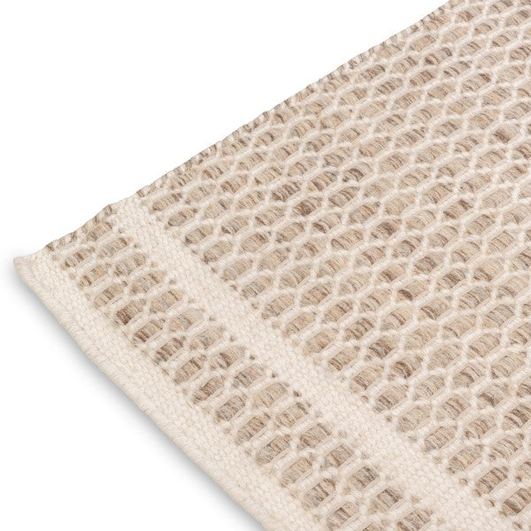 Close-up corner detail of the husk Theo wool rug showing the sturdy edge binding and the contrasting natural yarn colors.