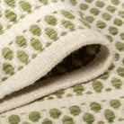 Soft draped folds of the sage green Theo wool rug showcasing its flexible woven geometric pattern.