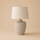 Table lamp with textured base and white shade on a beige background
