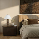 Neatly made bed with pillows, nightstand with lamp, and abstract wall art in a bedroom setting.