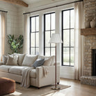 Valen floor lamp styled in a bright living room with high ceilings, standing next to a beige sofa.