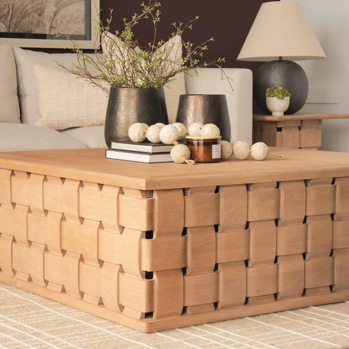 Angled lifestyle view of the Varelle Carved Mango Wood Square Coffee Table styled with books, vases and decorative accents.