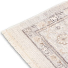 Corner view of the neutral Verona area rug highlighting its distressed floral border pattern, bound side edge, and short fringe detailing.