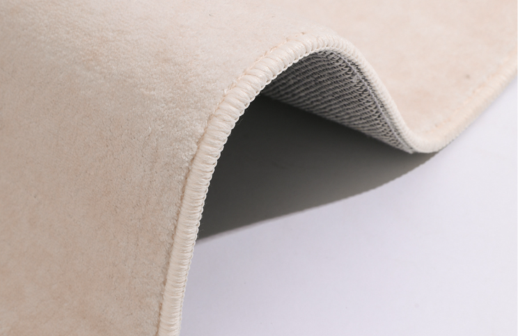 Close-up of the Woven Whisper Rug showing its soft beige surface, rounded edge, and flexible backing detail.